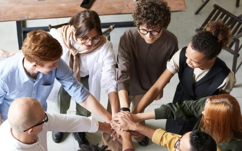 A diverse group of professionals joins hands in a team-building exercise indoors.