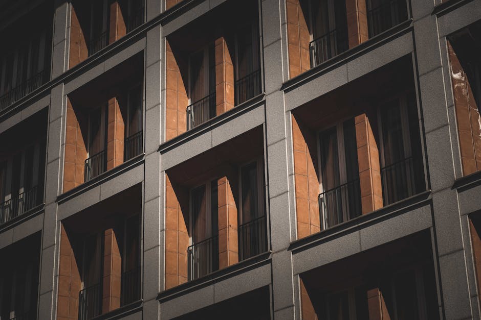Low angle of symmetric windows windows with French balconies of modern multistory residential building on sunny day in city